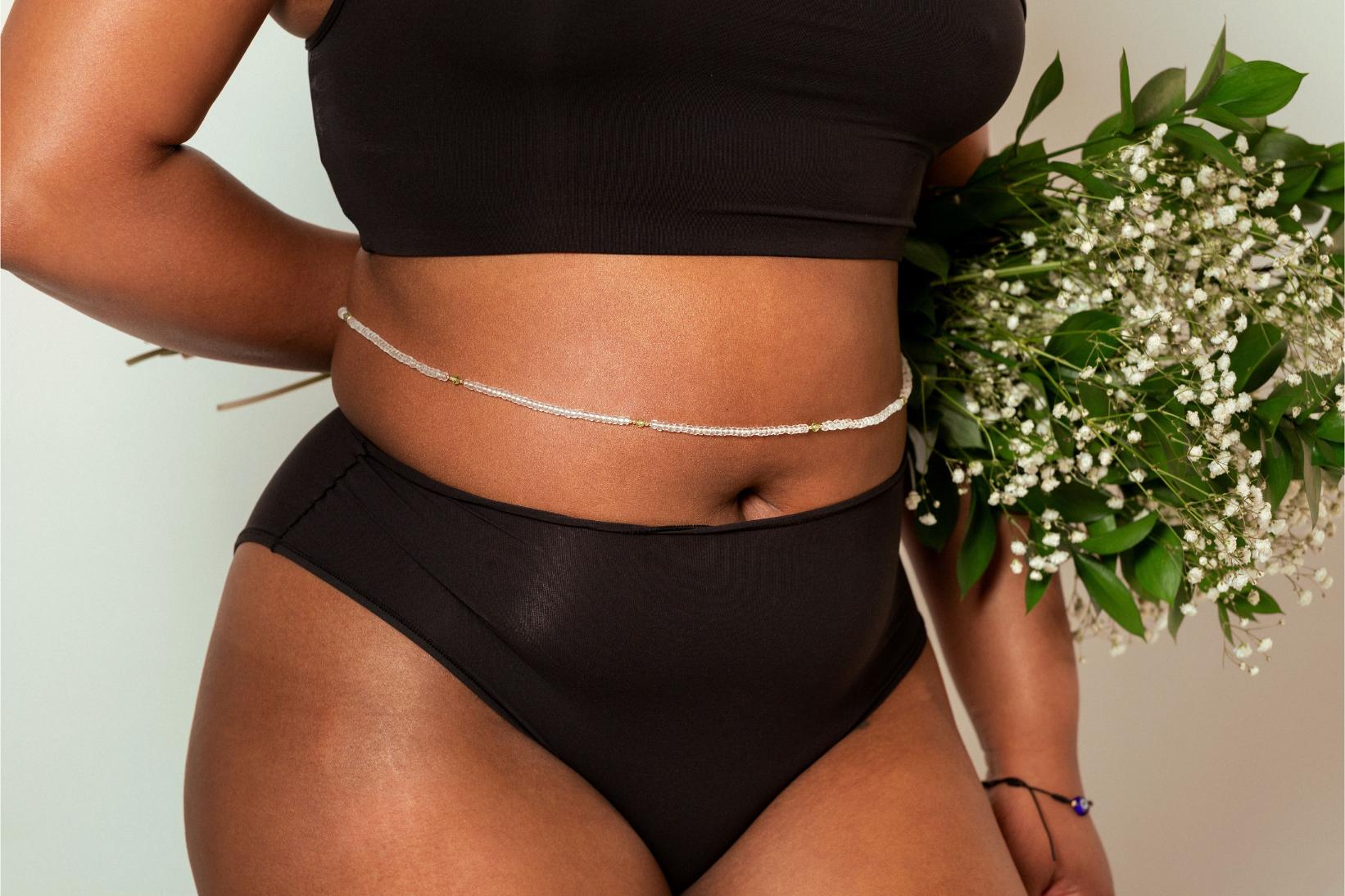Black female model wearing single strand of raine waistbeads and holding flowers
